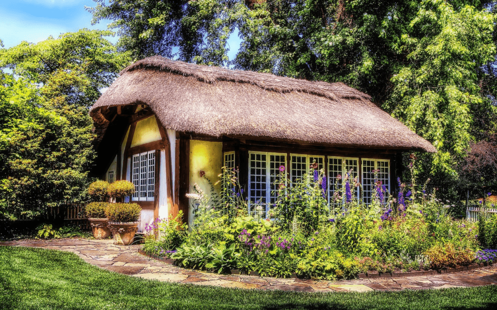 A quaint little cottage surrounding by ample and flourishing greenery and flowers with a stone path wrapped around the garden.