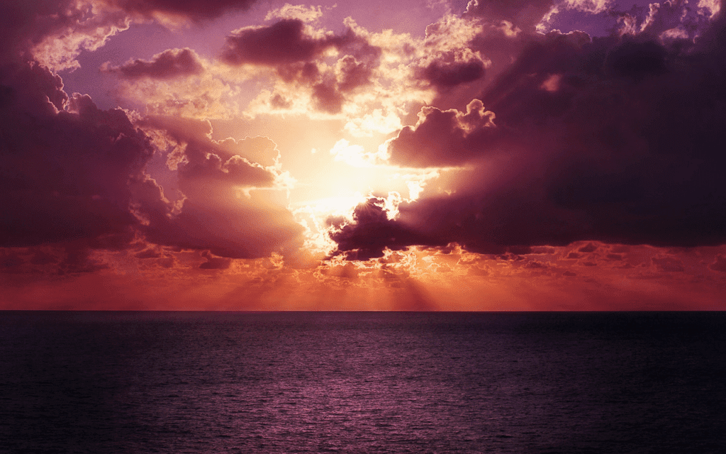 A cloudy sunset with bright sun rays over water.