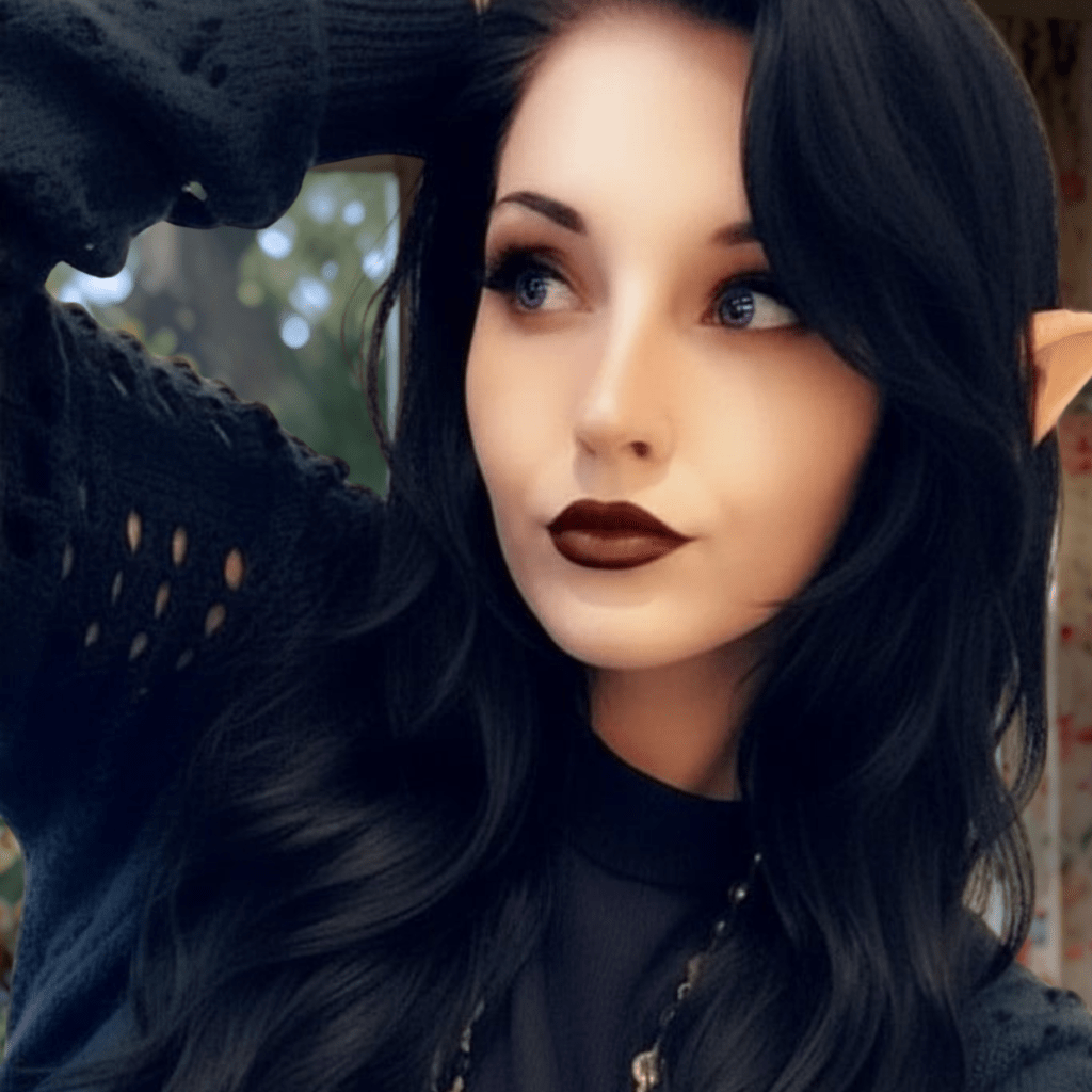 photograph of a young woman with wave black hair, lavender contacts, and prosthetic elf ears with her face turned to the left